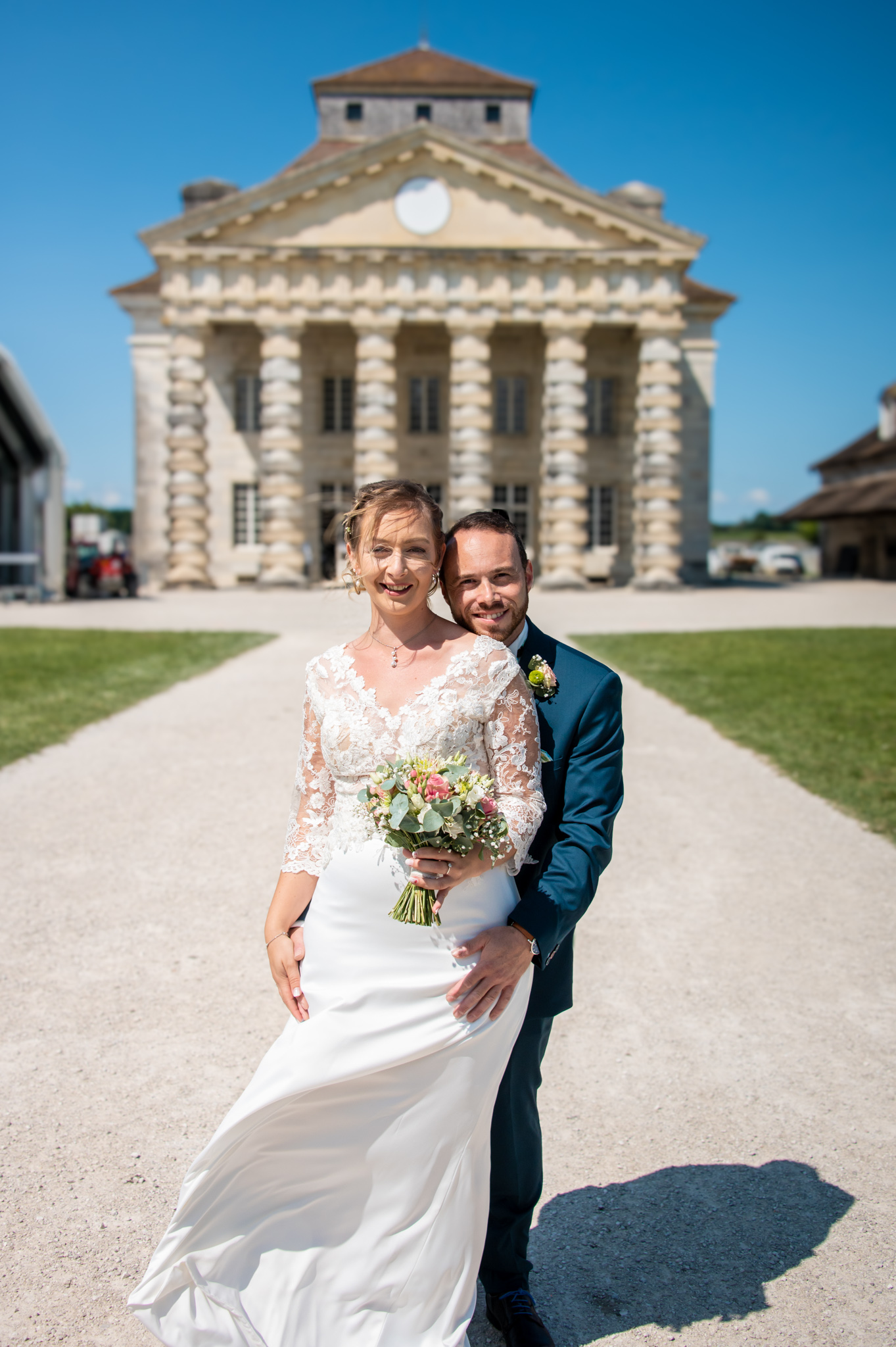 Mariés avec un bouquet devant les Salines d'Arc-et-Senans