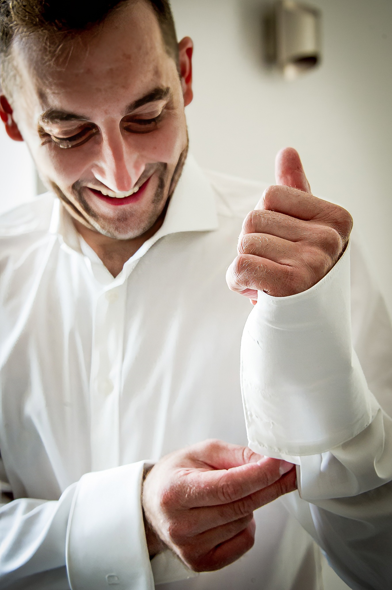 Le marié souriant en train de boutonner sa chemise blanche